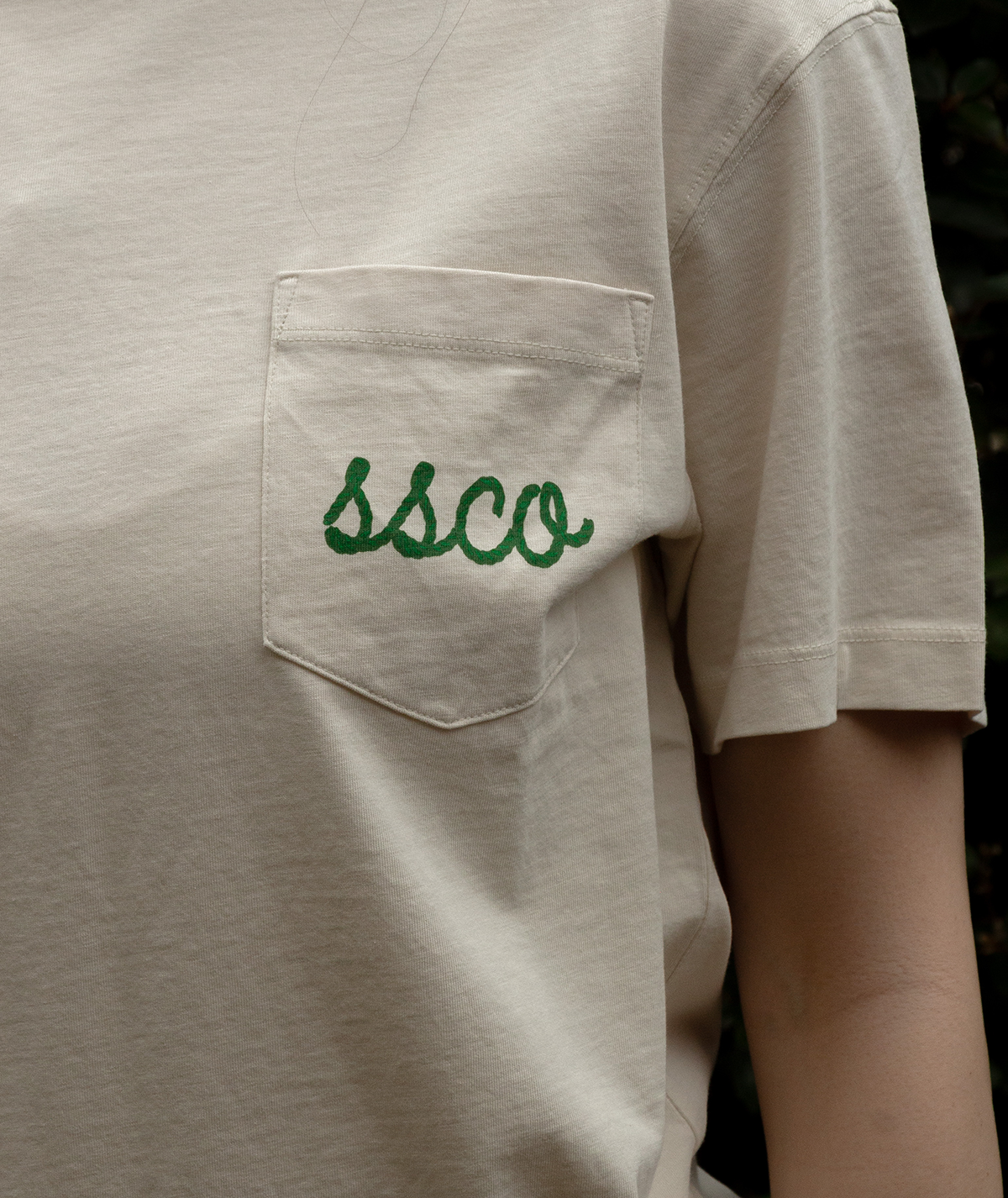 Close-up of a beige tee displaying embroidered 'ssco' on the pocket, showcasing the Feeling Lucky Tee SS design.