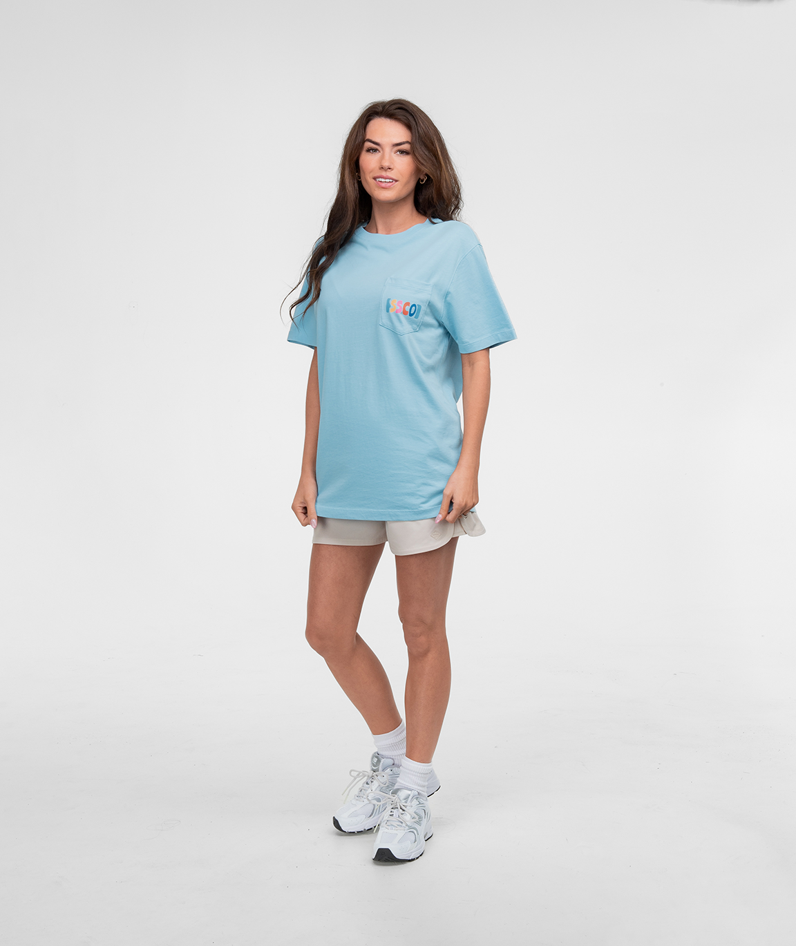Model wearing Pieces Of Paradise Tee SS in light blue, paired with shorts and sneakers, standing against a plain background.