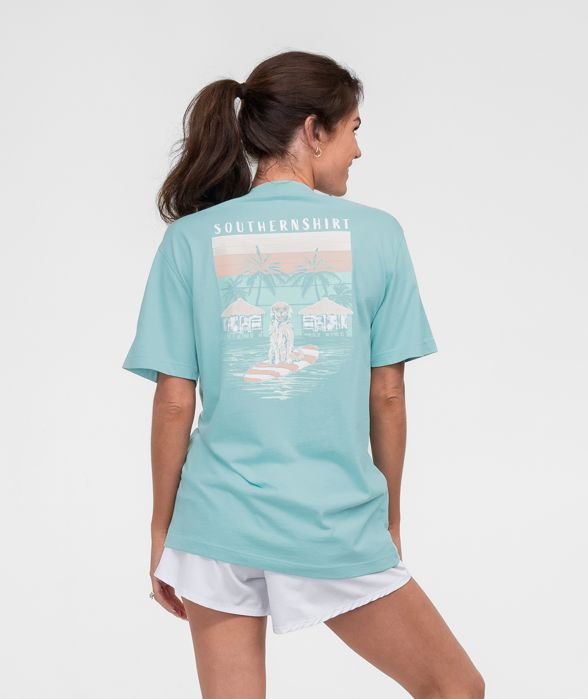 No Ruff Waters Tee SS featuring a woman wearing a teal shirt with a beach design on the back.