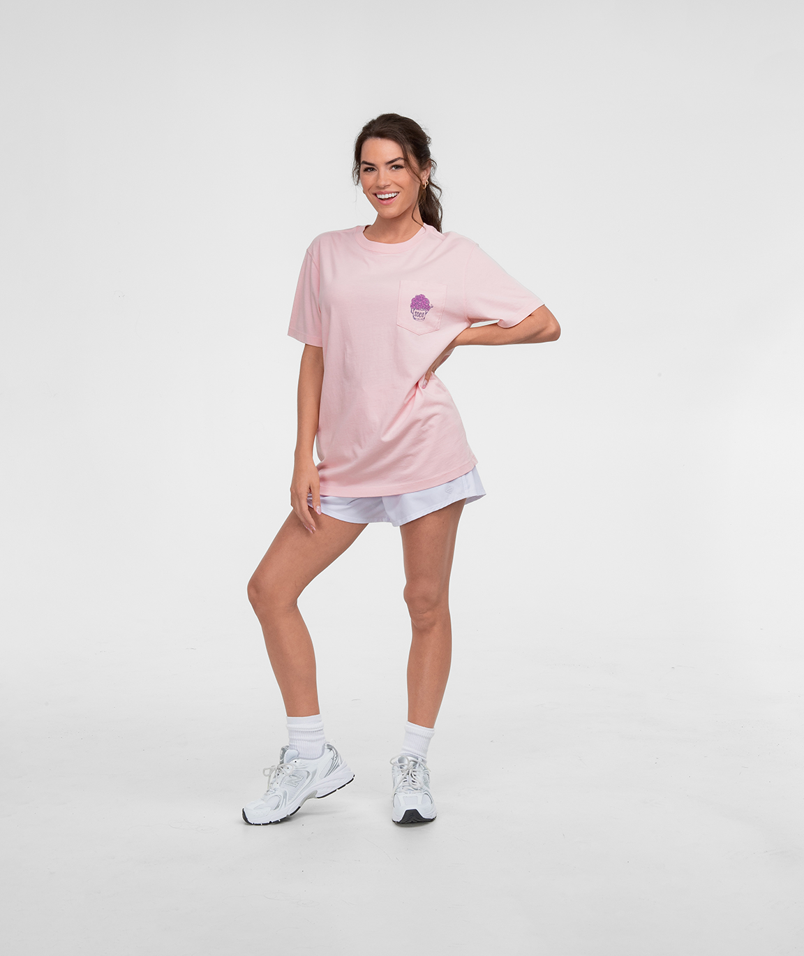 Woman wearing the Special Delivery Tee SS in pink, styled with shorts and sneakers, standing confidently.
