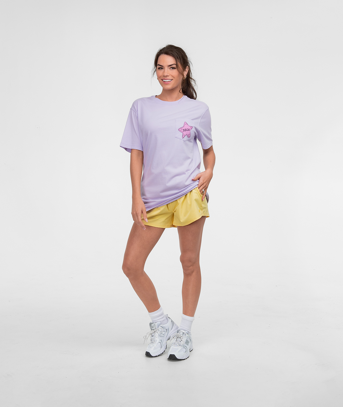 Model wearing Hotel Good Life Tee SS with yellow shorts and white sneakers on a plain background.