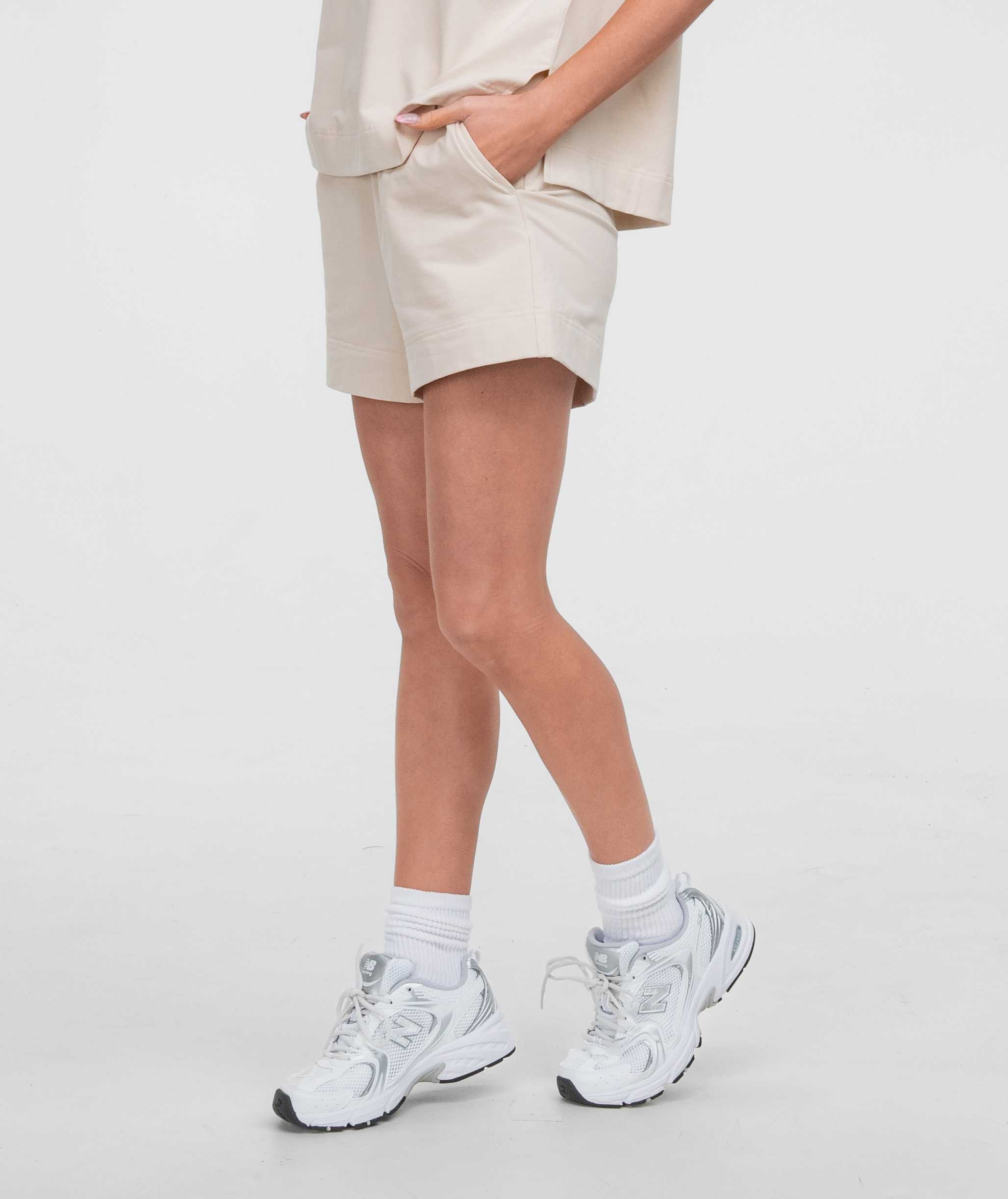 Model wearing Off Duty Shorts in beige color, paired with white sneakers and socks for a casual look.