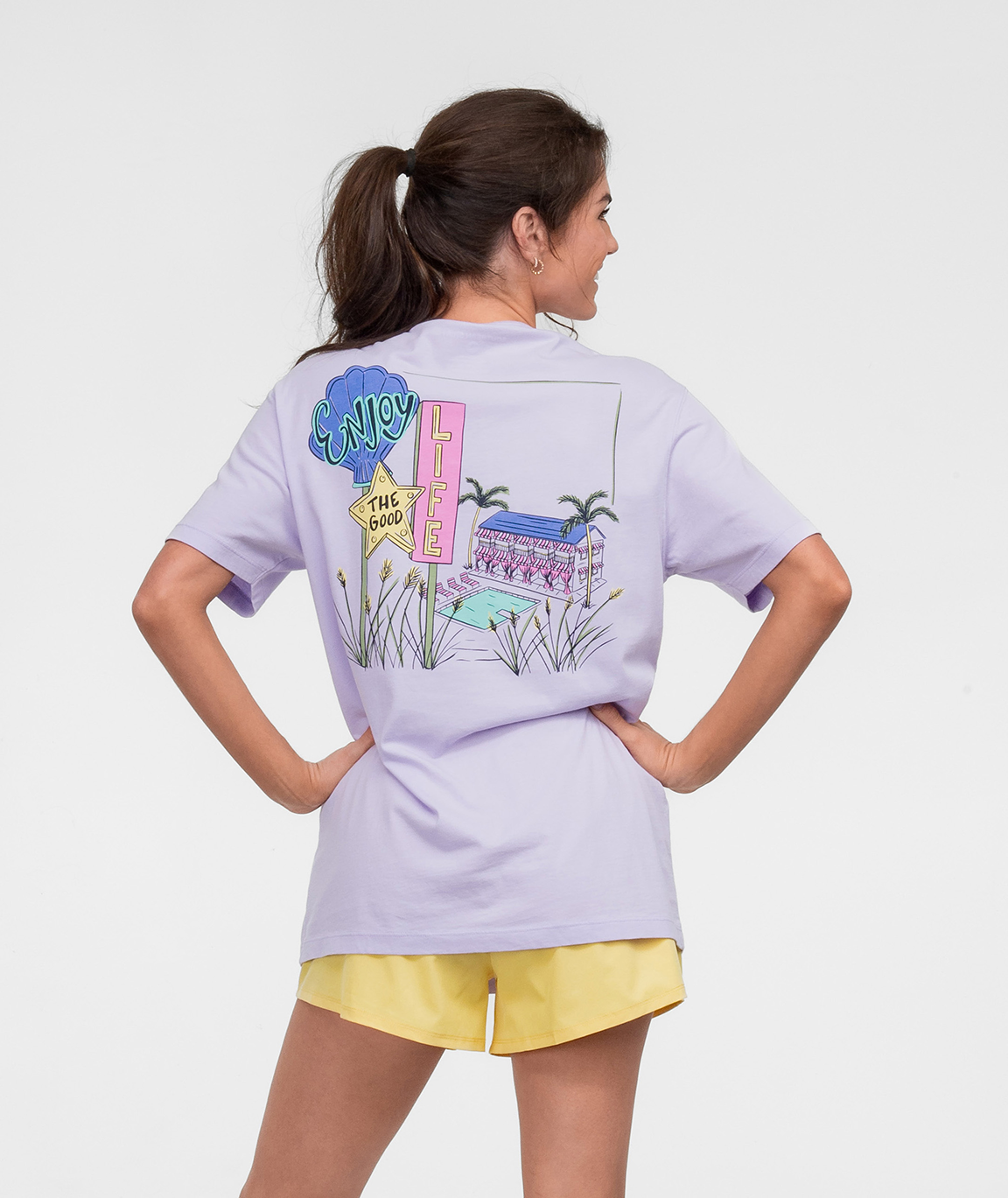 Model wearing the Hotel Good Life Tee SS in lavender with colorful graphic on the back.