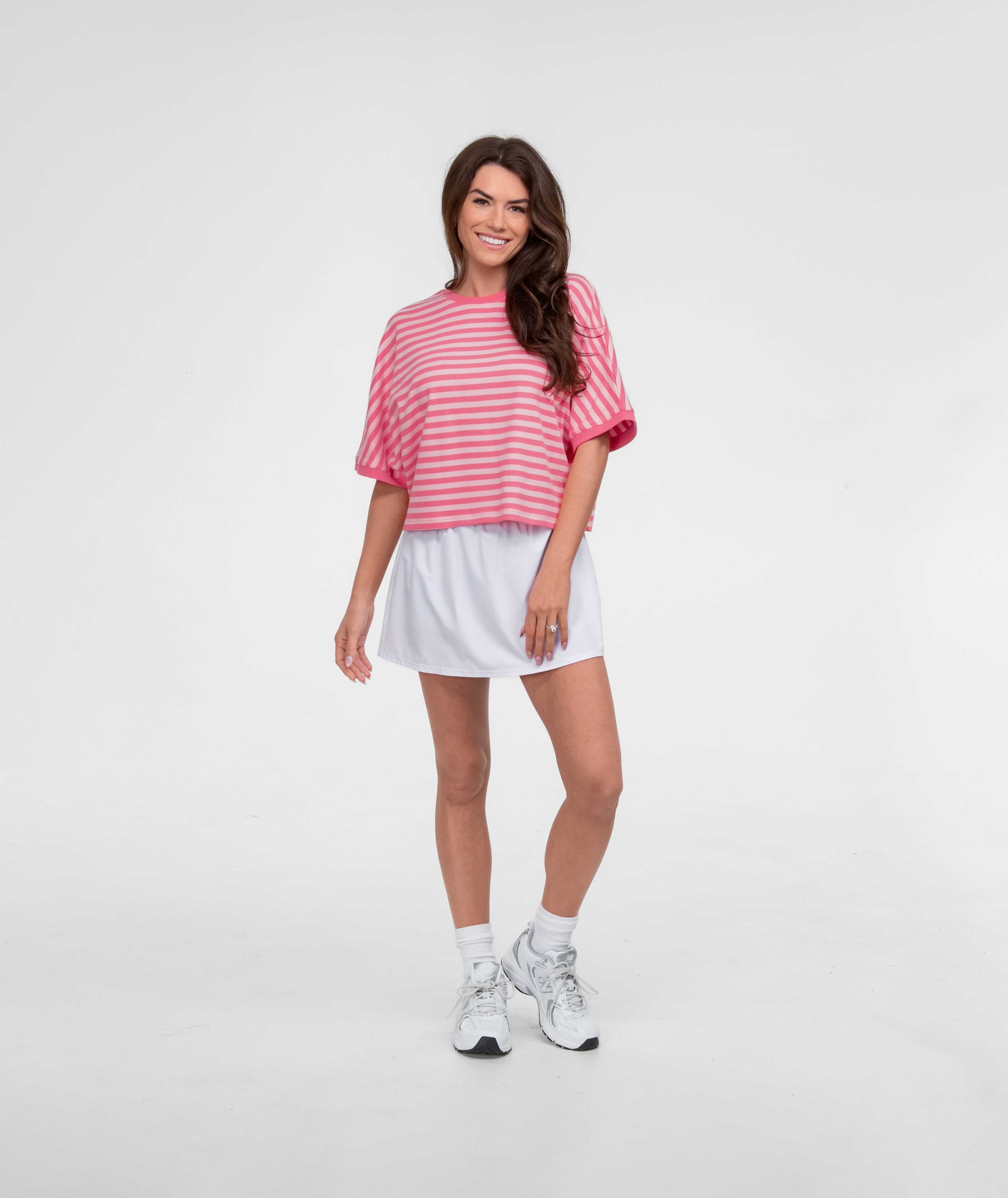 Model wearing the On The Line SS Top in pink stripes with a white skirt and sneakers.