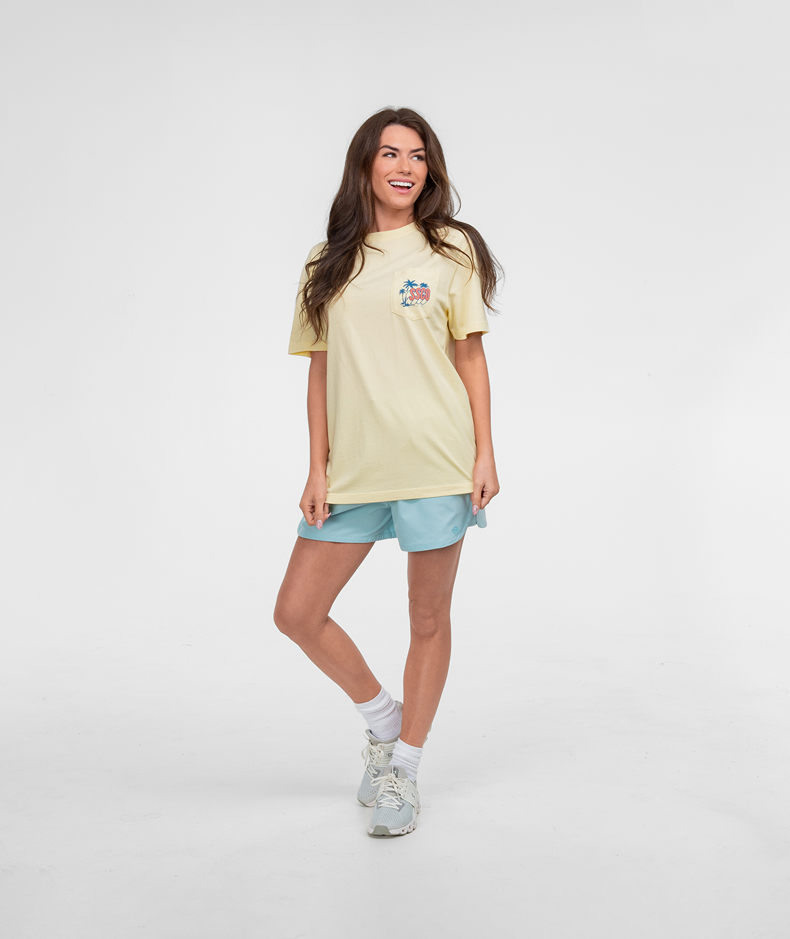 Model wearing a casual Mental Vacation Tee SS in yellow with light blue shorts, smiling against a white background.